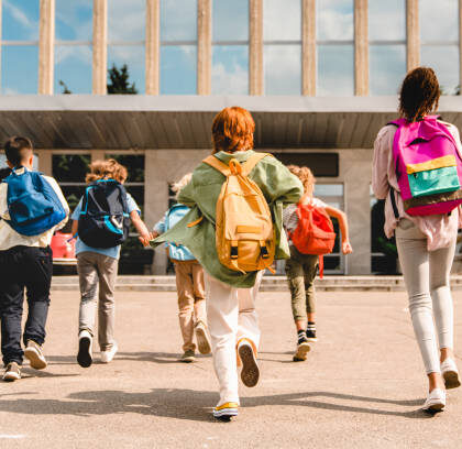 Little kids schoolchildren pupils students running hurrying to the school building for classes lessons from to the school bus. Welcome back to school. The new academic semester year start